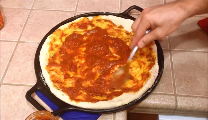 Remove from oven, add pizza sauce, mozzarella cheese, pepperoni, olives, sautéed bell peppers, fresh basil, jalapenos, and more mozzarella cheese.