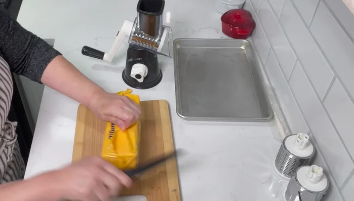 Cut the block of cheese into smaller pieces that fit into the grater's feeding tube.